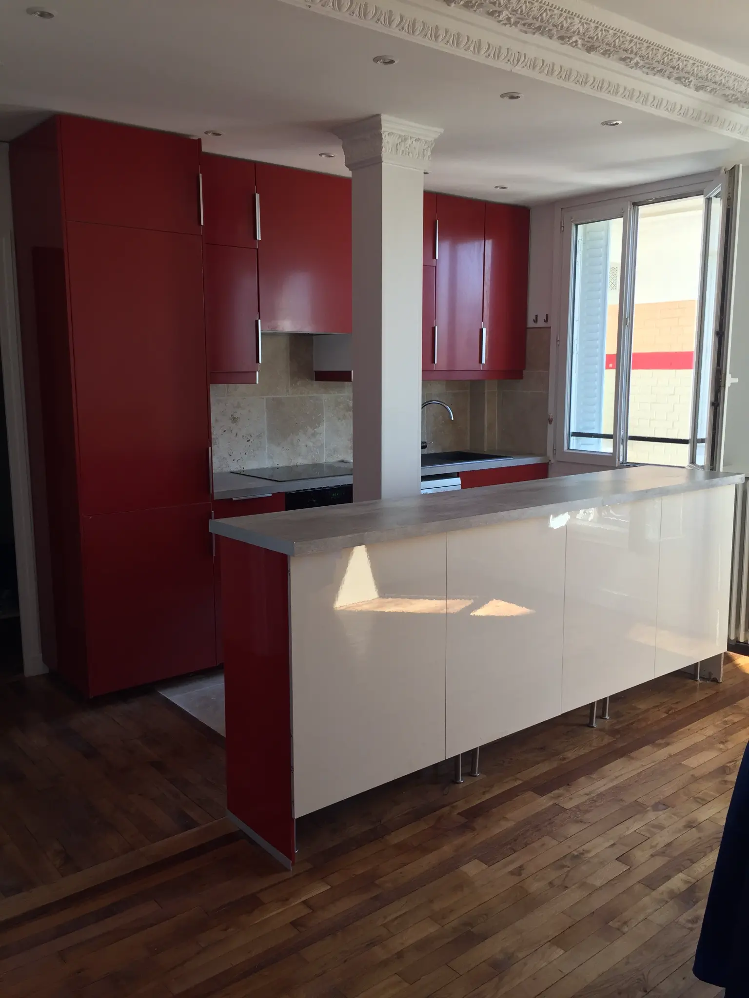 Cuisine ouverte avec façades rouges, bar blanc et sol en bois