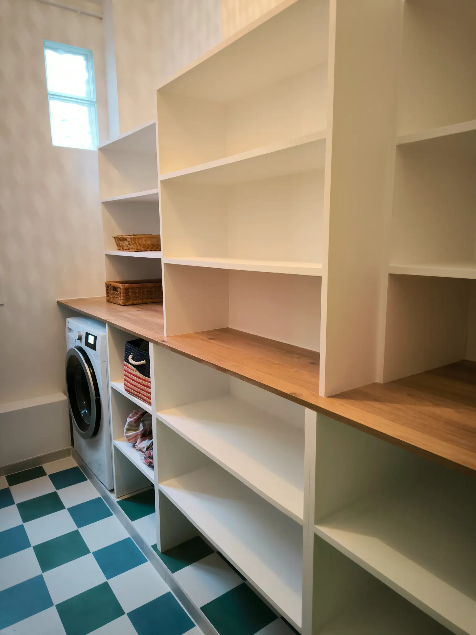 Rangement blanc sur mesure avec tablette bois, espace buanderie et sol à carreaux vert et blanc